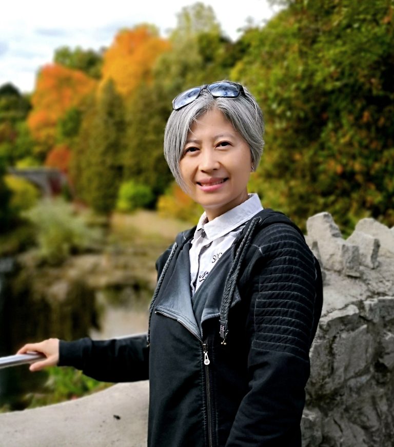 Smiling woman with short gray hair standing outdoors by a stone railing