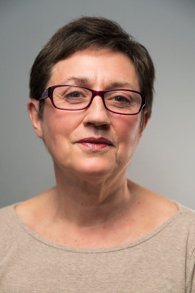 Head-and-shoulders portrait of a woman with short hair and glasses against a gray background.