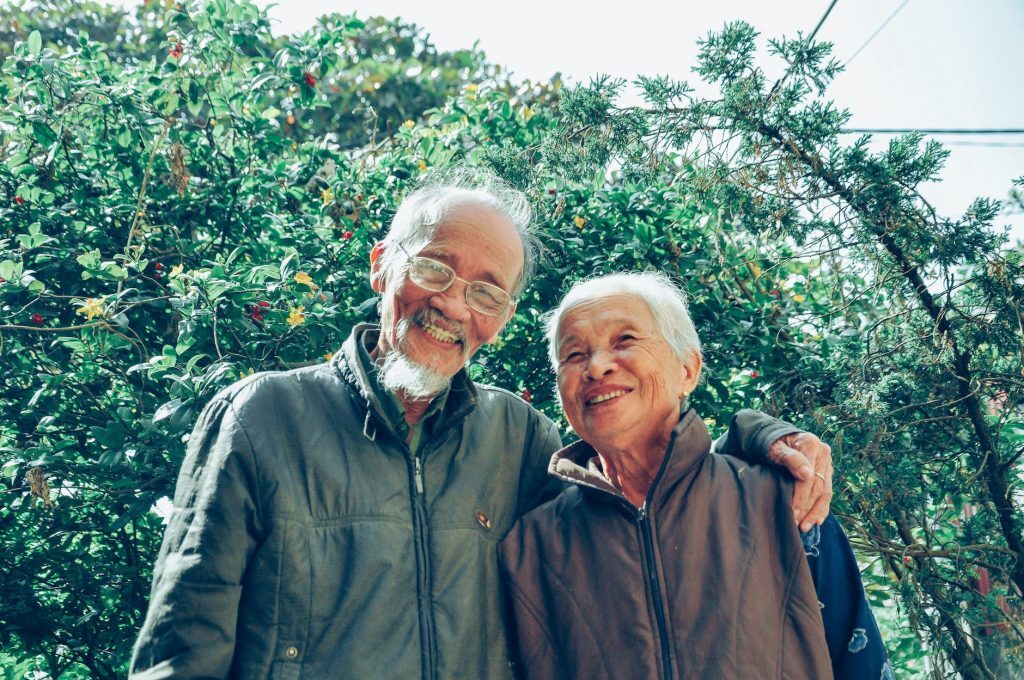 Smiling older couple standing outdoors among green plants