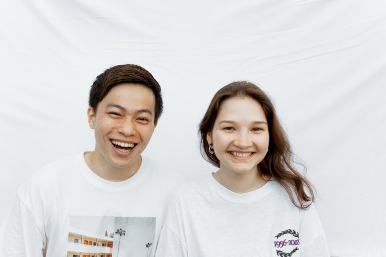 Two smiling young adults in white T-shirts against a white background.