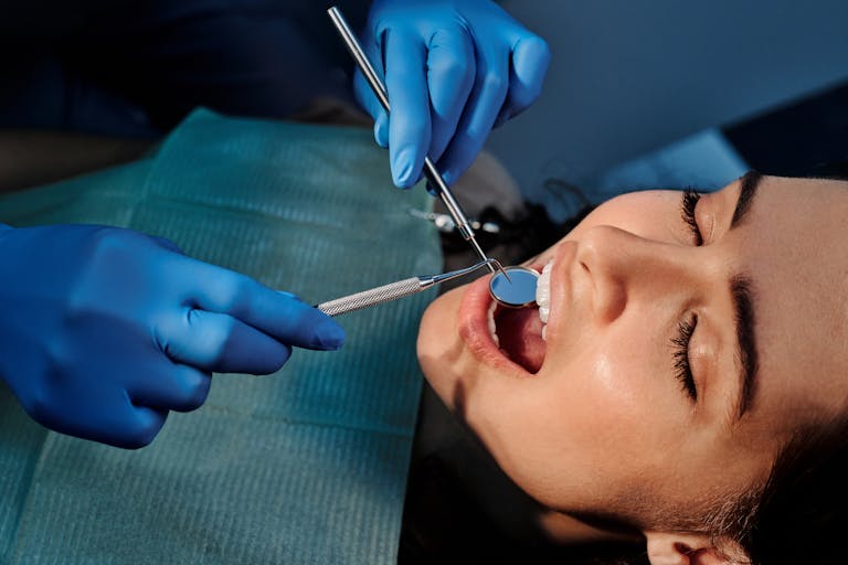 Dentist examining a reclining patient's teeth with a mirror and scaler.