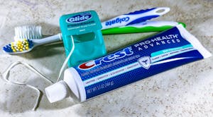 Close-up of toothbrushes, dental floss, and a toothpaste tube on a countertop.