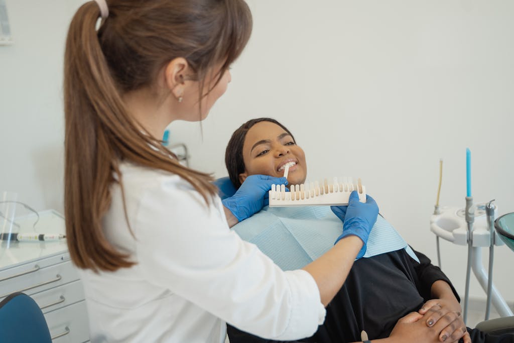 Dentist comparing a tooth shade guide with a smiling patient in a dental chair.
