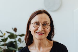 Smiling senior woman wearing round glasses in a bright indoor portrait.