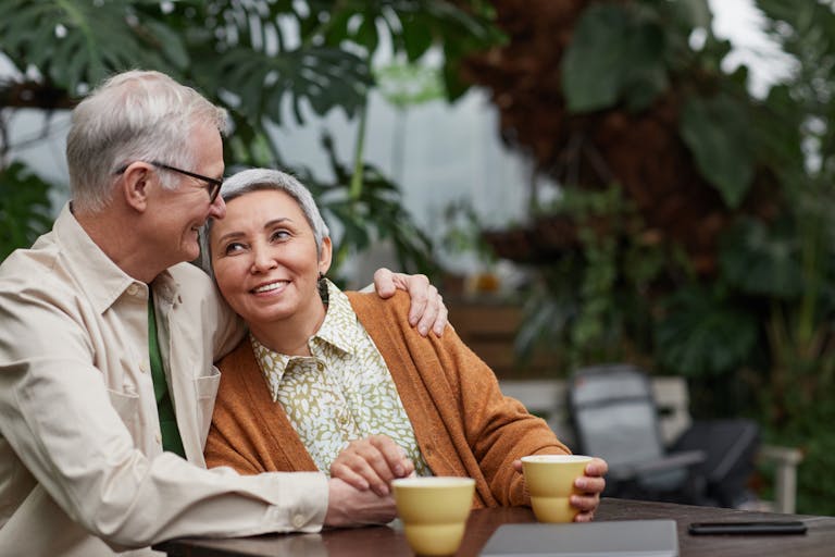 Smiling older couple sitting together outdoors with coffee cups.