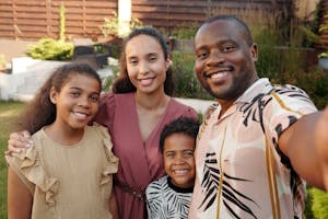 Smiling family of four taking a selfie together outdoors in a garden.