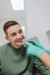 Smiling teenage boy during a dental shade comparison with a dentist holding a tooth shade guide.