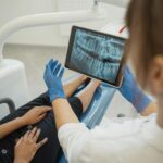 Dentist showing a dental x-ray on a tablet to a patient in a dental chair.