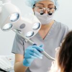 Dentist examining a patient with dental tools and overhead exam light in a modern clinic.