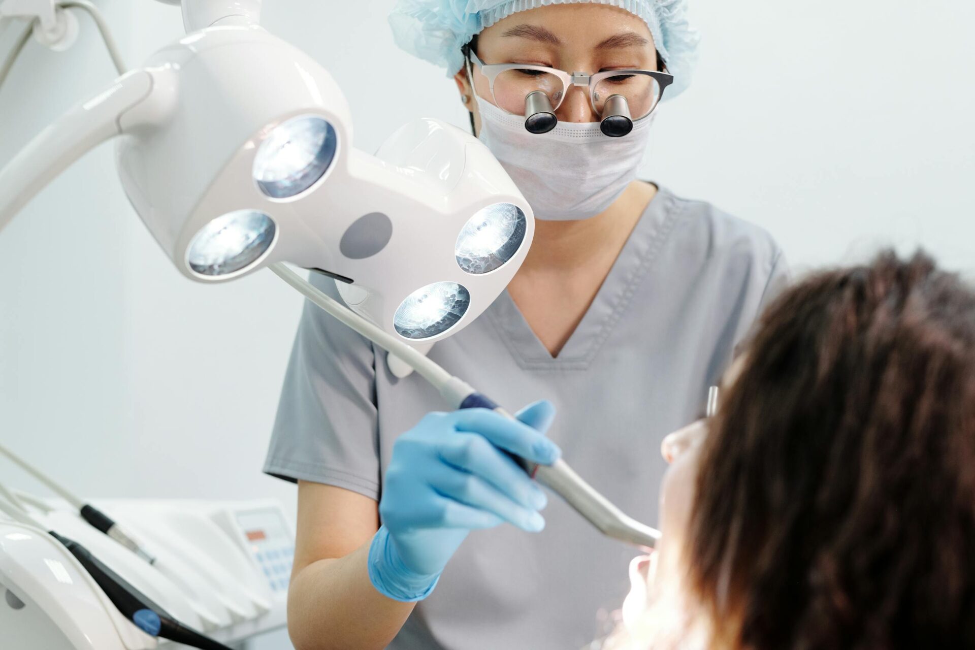 Dentist examining a patient with dental tools and overhead exam light in a modern clinic.